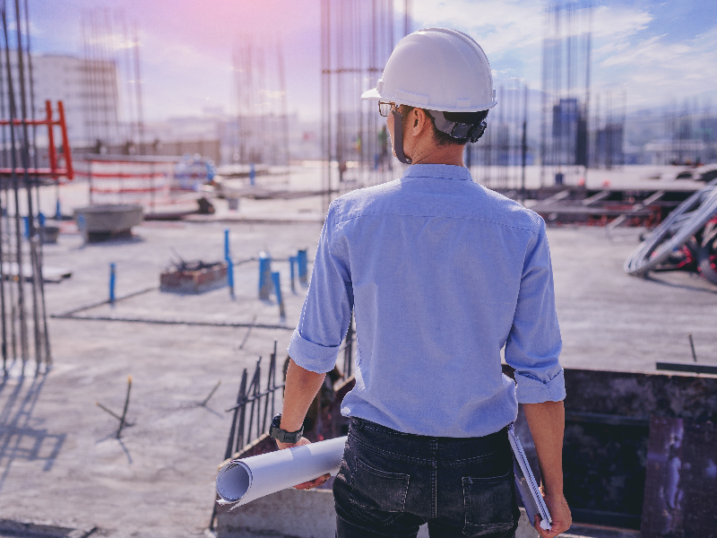 Architect holding rolled-up blueprints while looking over a building site. Marketing to Architects: Inbound Resources for Product Manufacturers