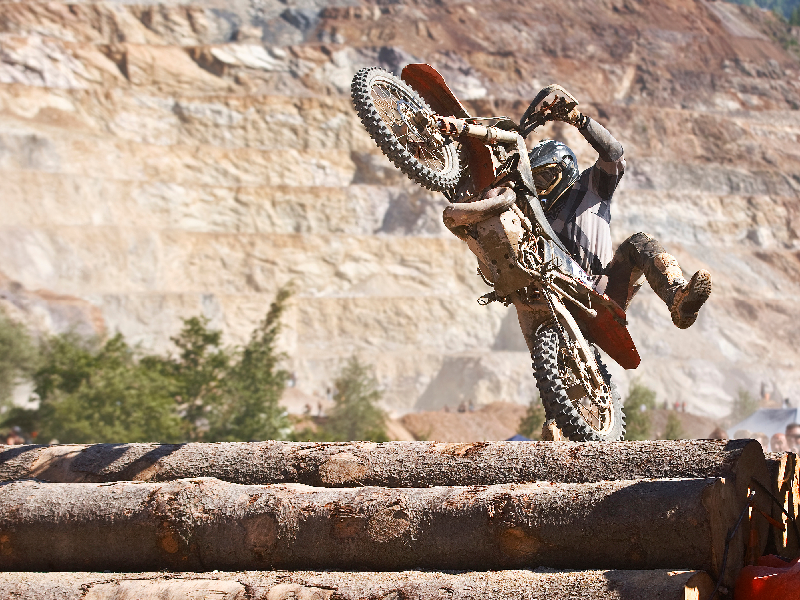 A competitor in the Erzbergrodeo rides over logs. Their bike is in a wheelie position. Conquering the World's Wildest Dirt Bike Race: The Erzbergrodeo [VIDEO]