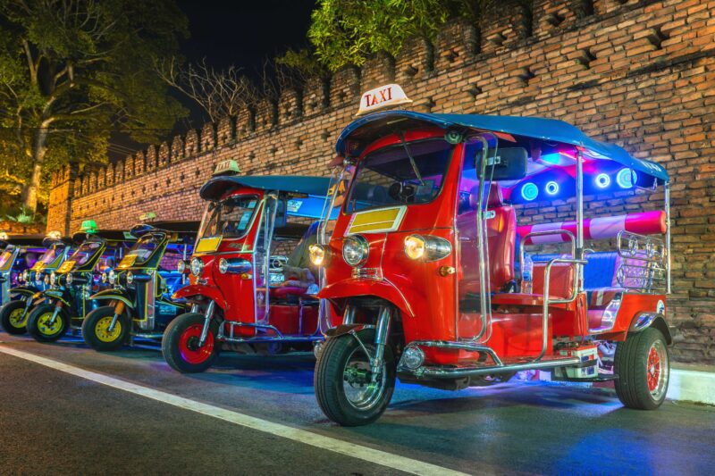 A line of brightly colored, brightly lit tuk-tuks sit in a line at night. Engineering a Wacky Auto Race: What is Tuk-Tuk Racing?